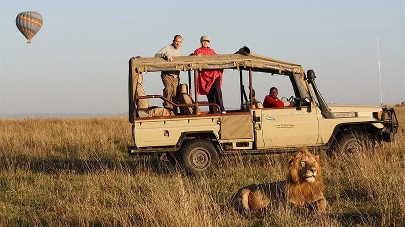 Safari vehicle on the Kenyan plains with a balloon in the distance